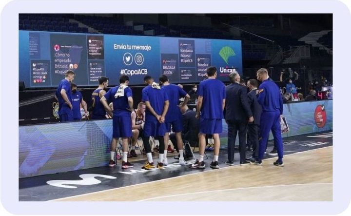 Courtside LED screen at a Copa ACB basketball game running an audience activation platform that displays fan tweets and Instagram posts with the #CopaACB hashtag.