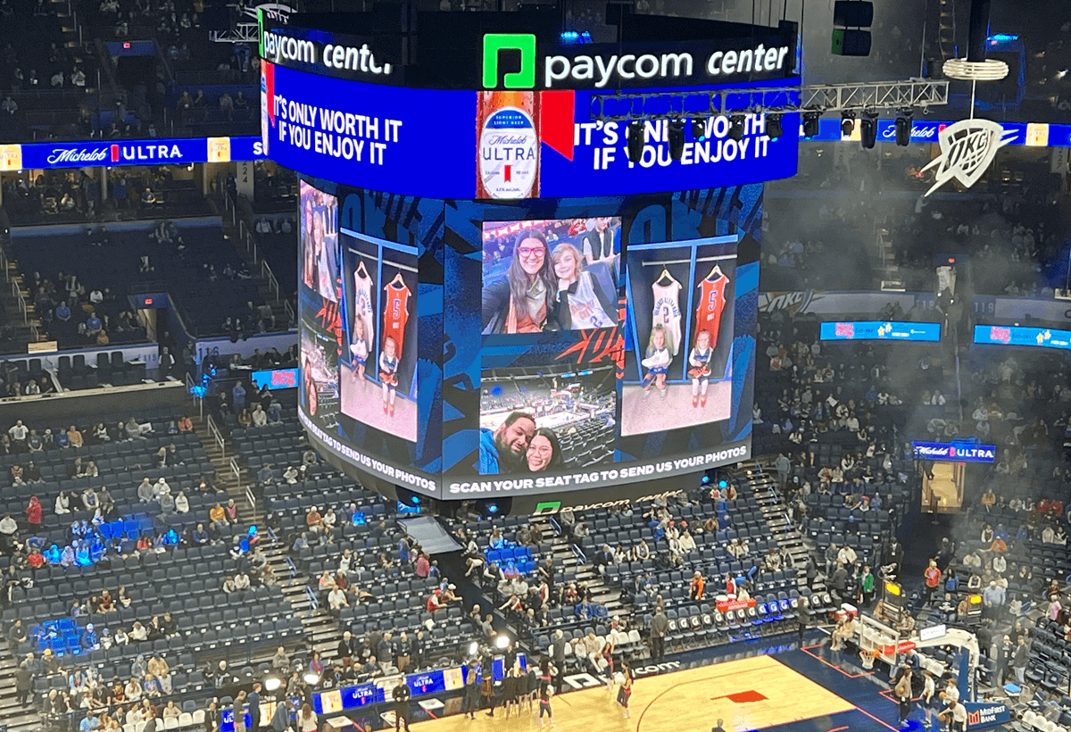 Fan photos displayed on the jumbotron at Paycom Center during an Oklahoma City Thunder game, with a prompt encouraging fans to scan their seat tag to submit content.
